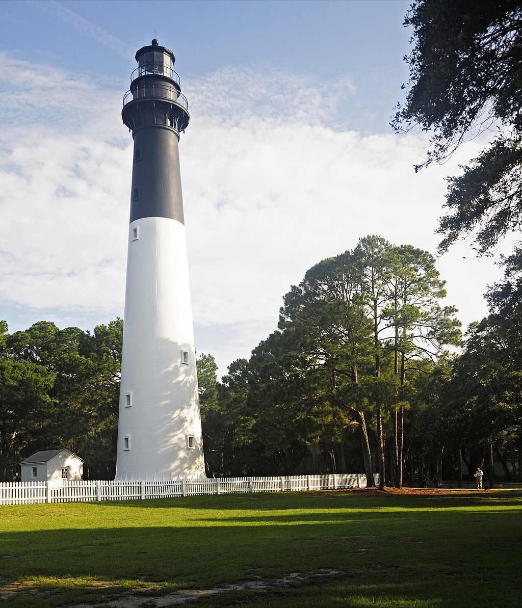 Hunting Island Lighthouse above a white fence and coastal trees